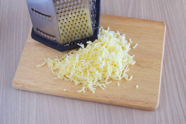 Step by step cooking. Grated mozarella cheese with a grater on a wooden cutting board on a grey background Step by step cooking. Grated mozarella cheese with a grater on a wooden cutting board on a grey background shredded mozzarella stock pictures, royalty-free photos & images