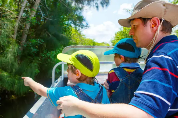 Two little kids boys and father making air boat tour in Florida wetland swamp at Everglades National Park in USA. Family, dad and children discovering wild nature and animals. Family having fun.