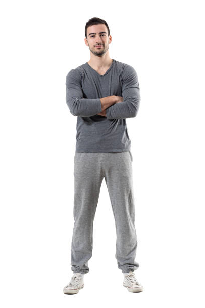 Positive smiling young fit sporty man with crossed arms looking at camera. Positive smiling young fit sporty man with crossed arms looking at camera. Full body length portrait isolated on white studio background. jogging pants stock pictures, royalty-free photos & images