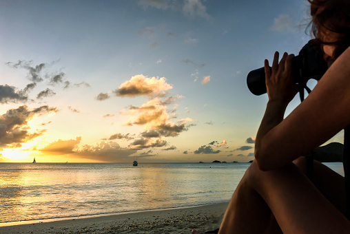 A bikini woman photographer adjusts the zoom lens to capture a beautiful beach sunset at tropical island