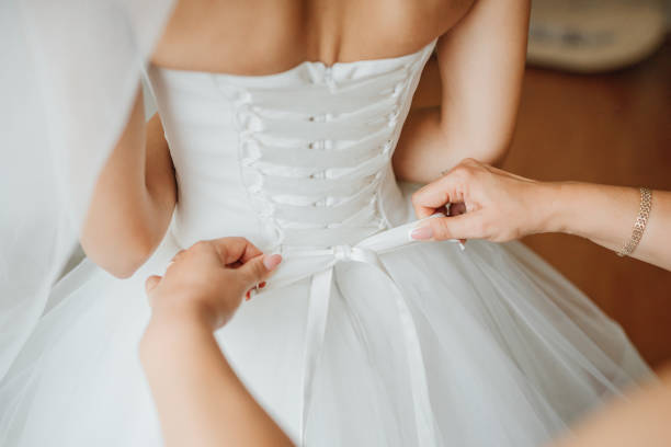 Bridesmaid makes bow-knot on the back of brides wedding dress Bridesmaid makes bow-knot on the back of brides wedding dress wedding dresses stock pictures, royalty-free photos & images