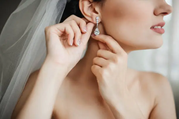 Photo of Wedding preparation. Beautiful, happy bride dresses earrings before wedding. Wedding accessories, jewelry. Closeup portrait of bride. Selective focus.