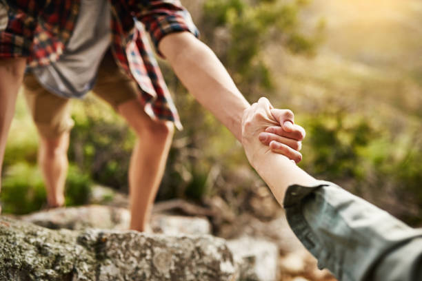 Alone we climb rocks, together we climb mountains Cropped shot of hikers helping each other climb up a rock in nature pulling stock pictures, royalty-free photos & images