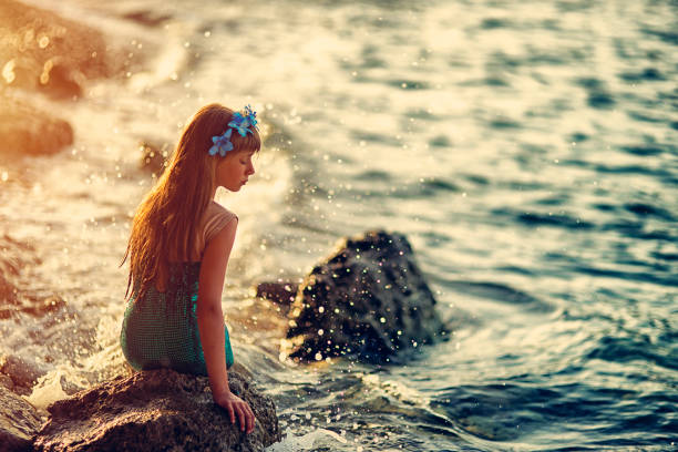 Little mermaid sitting on the rock at the sea shore.\n\n