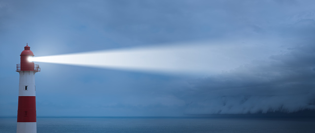 The Punta Nariga Lighthouse on the cliff under the sunrays piercing through the cloudy sky in Spain