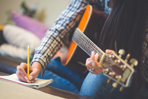 Close up of girls hand writing down music, playing a guitar. Shallow DOF, focus on hand and pencil.