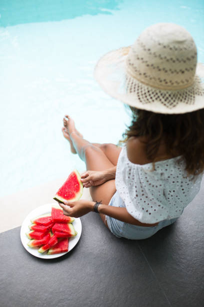 istock Young Pretty Woman Eating Watermelon on Pool Edge 680660280