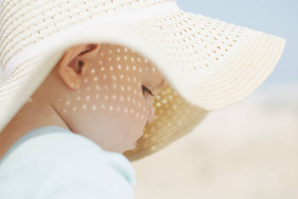 Cute baby girl with blue dress and straw hat enjoying a calm morning at the beach.