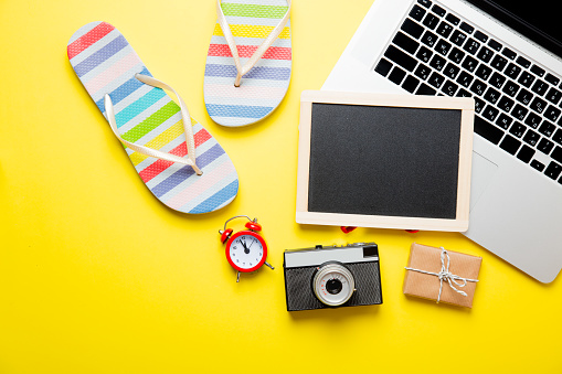 photo of empty blackboard, colorful sandals, retro camera, alarm clock, cute gift and cool laptop on the wonderful yellow studio background