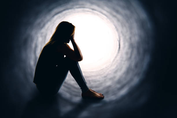 Woman Depressed And Alone A depressed woman sitting alone is a dark tunnel with light at the other end. bipolar disorder stock pictures, royalty-free photos & images