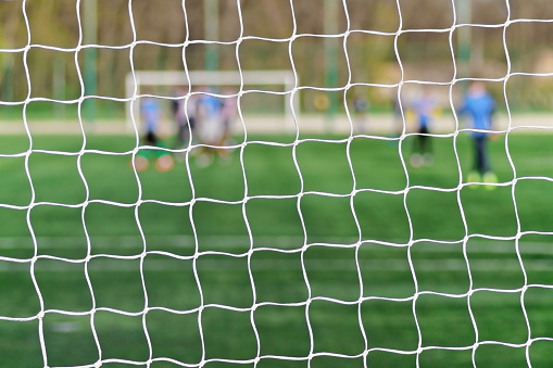 Behind goal of soccer field. Soccer football net background over green grass or soccer field and blurry stadium and soccer players. Football, soccer field.
