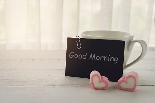 Cup of coffee and heart shape candy with note on wooden table