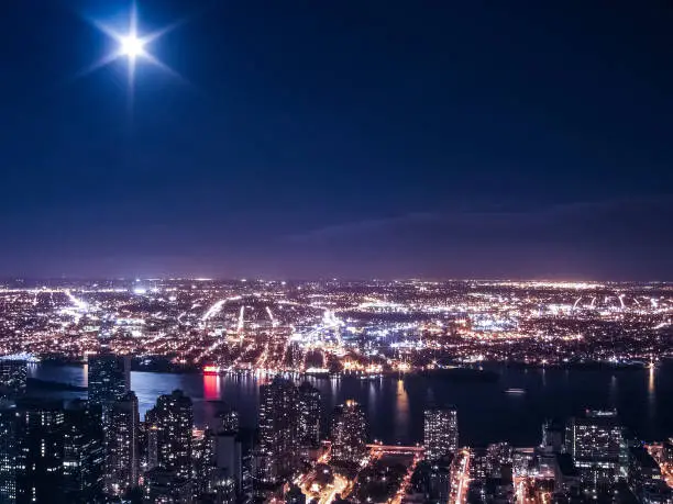 View of night cityscape or skyline of New York City with moon and illuminated buildings and Hudson River from Empire State Building