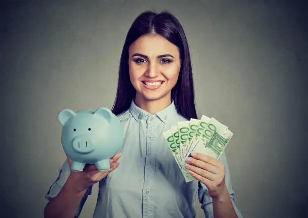 Photo of woman smiling, holding piggy bank and hundred euro banknotes