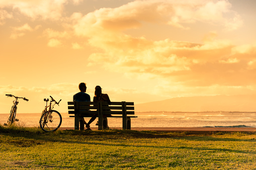 Couple sitting on park bench watching the beautiful sunset in Hawaii.