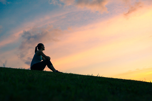Young woman sitting outdoors watching sunset.
