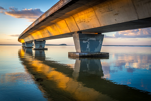 sunset shining on highway bridge with beautiful reflection of bridge in glassy water