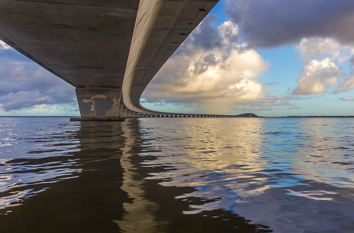 abstract view of highway bridge with cumulus clouds and bridge reflecting in calm water
