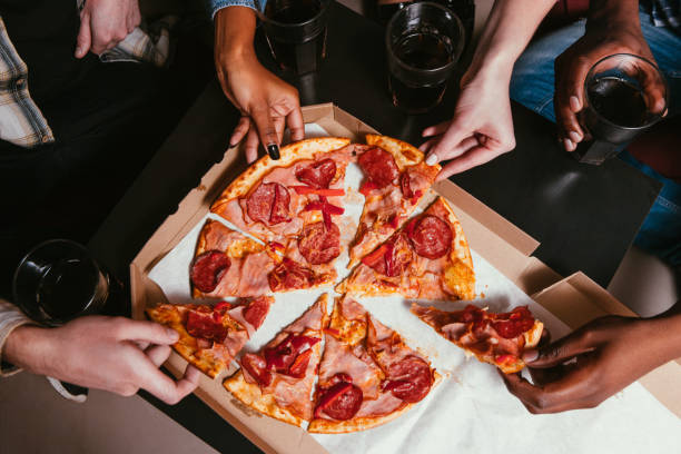 cuatro amigos de la empresa comen pizza fresca en casa - pizza party fotografías e imágenes de stock