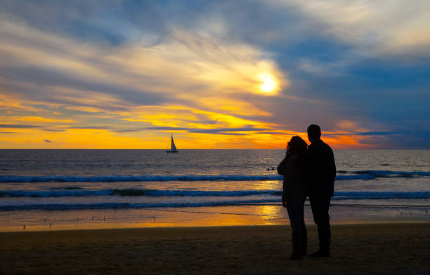 Romantic couple on the beach  looking at the sailboat at sunset