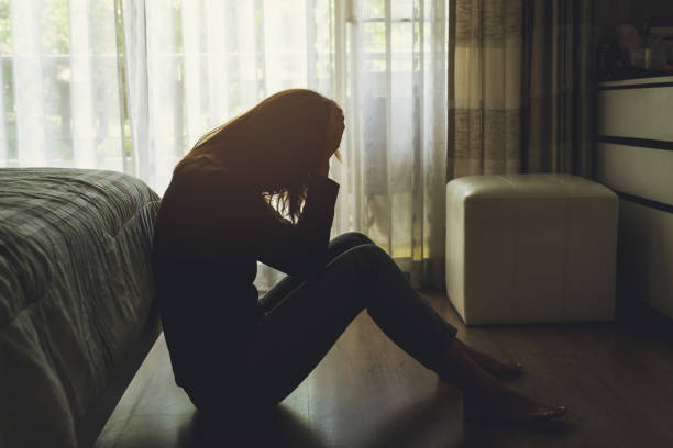 mujer deprimida sentada en el dormitorio oscuro - tristeza fotografías e imágenes de stock