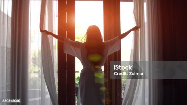 Mujer Joven En Bata De Baño Abra Cortinas Y Estirar De Pie Cerca De La Ventana En Su Casa Foto de stock y más banco de imágenes de Hotel