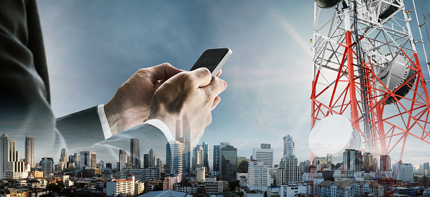 Double exposure businessman using smartphone with cityscape, and telecommunication towers