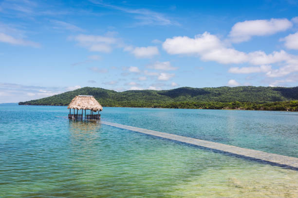 Flooded underwater jetty with straw hut leading into Lake Petén Itzá under blue summer sky close to the city of Flores in Guatemala. Flores, Lake Petén Itzá, Guatemala, Central America