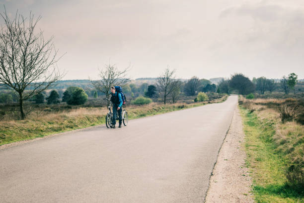istock Tourist with backpack walking with bicycle on road in moorland. 680873676