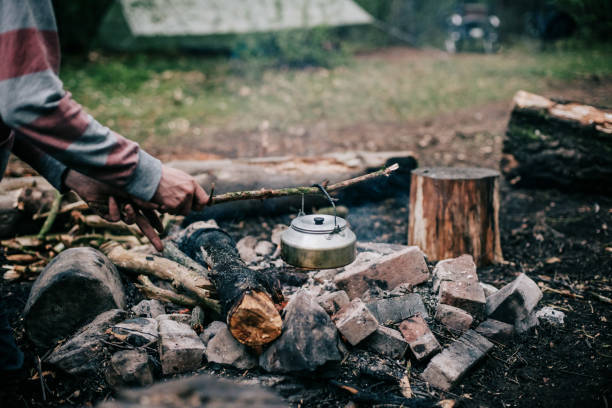 istock Male hand picking up hot kettle from campfire with branch. 680873782