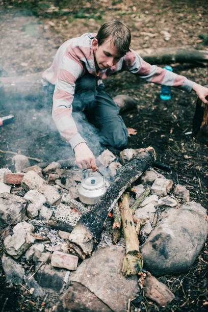 istock Man putting metal kettle into campfire. High angle view. 680873798