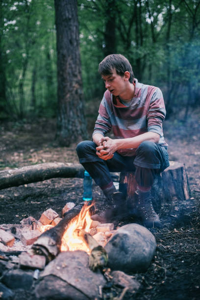 istock Traveler sitting on tree stump at campfire enjoying the warmth. 680873844