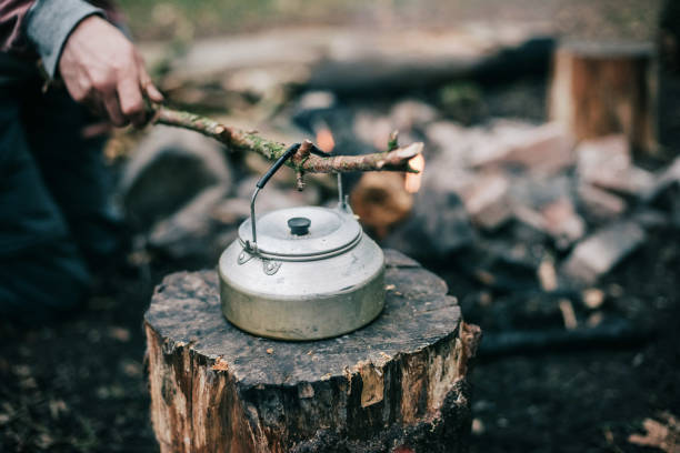 istock Male hand picking up hot kettle from campfire with branch. 680873854