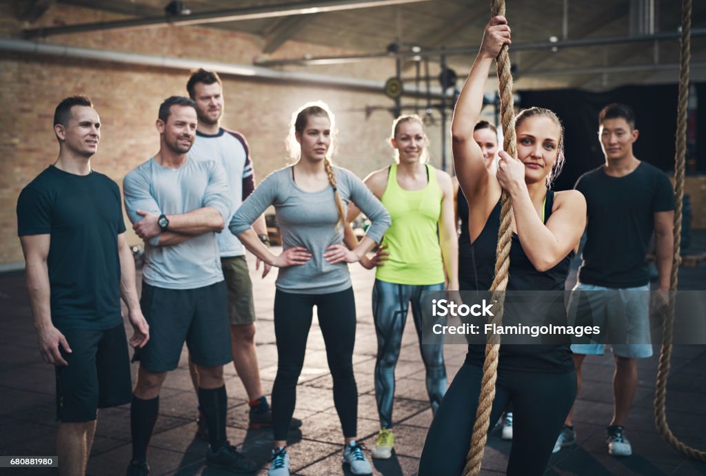 Woman holding climbing rope in gym exercises Group of adults watching woman use climbing rope in fitness exercise circuit training regimen Active Lifestyle Stock Photo