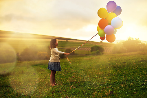 Shot of a playful little girl walking through a field while holding a bunch of balloons