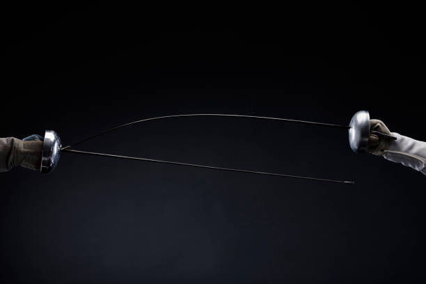 Fencing swords crossed. Close-up shot. Épée and Sabre type of fencing weapon. Dark black background. Fencing sport competition Duel Fencing swords crossed. Close-up shot. Épée and Sabre type of fencing weapon. Dark black background. Fencing sport fencing sport stock pictures, royalty-free photos & images