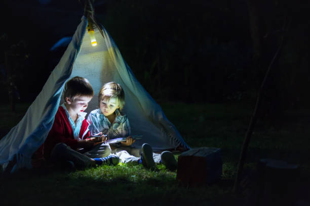 かわいい弟、夜テントの中で、campside のタブレットと電話で遊んで - シークレット 人 ストックフォトと画像