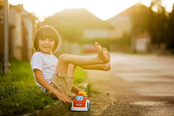 Photo of Cute sweet child, boy, playing with car toys on the street in village on sunset, summertime