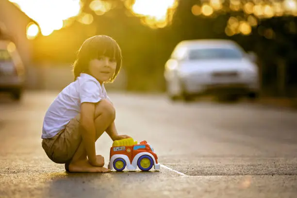 Photo of Two sweet children, boy brothers, playing with car toys on the street in village on sunset, summertime