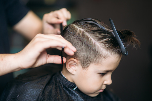 Niño que corte de pelo por el peluquero mientras estaba sentado en la silla de la barbería. photo