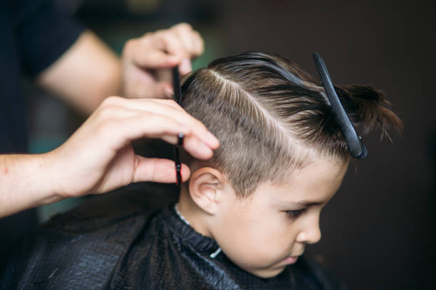 garotinho, cortar o cabelo por barbeiro enquanto está sentado na cadeira de barbearia. - salão de beleza - fotografias e filmes do acervo