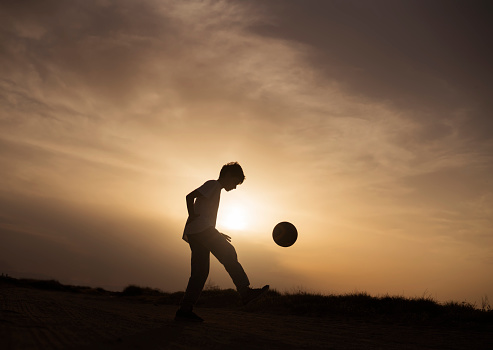 Boy playing football at sunset on the beach