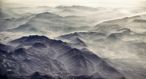 Fog rolling in the valleys between mountain peaks, photographed from the air.
