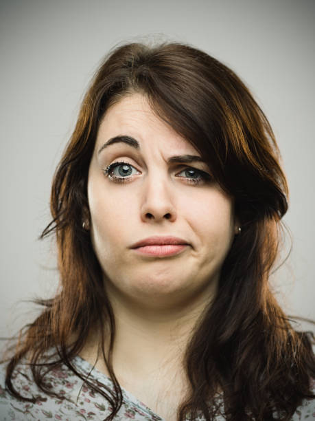 Annoyed young female against gray background Close up portrait of annoyed young female against gray background. Vertical shot of beautiful real woman looking upset. Studio photography from a DSLR camera. Sharp focus on eyes. confused face stock pictures, royalty-free photos & images