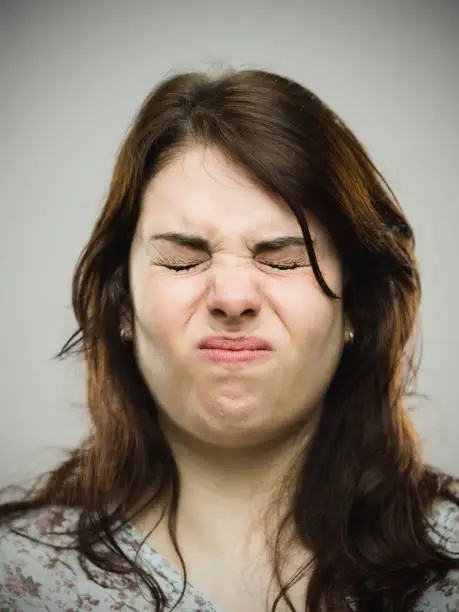 Close up portrait of angry woman puffing cheeks on gray background. Vertical shot of real woman feeling uncomfortable and stressed. Studio photography from a DSLR camera.