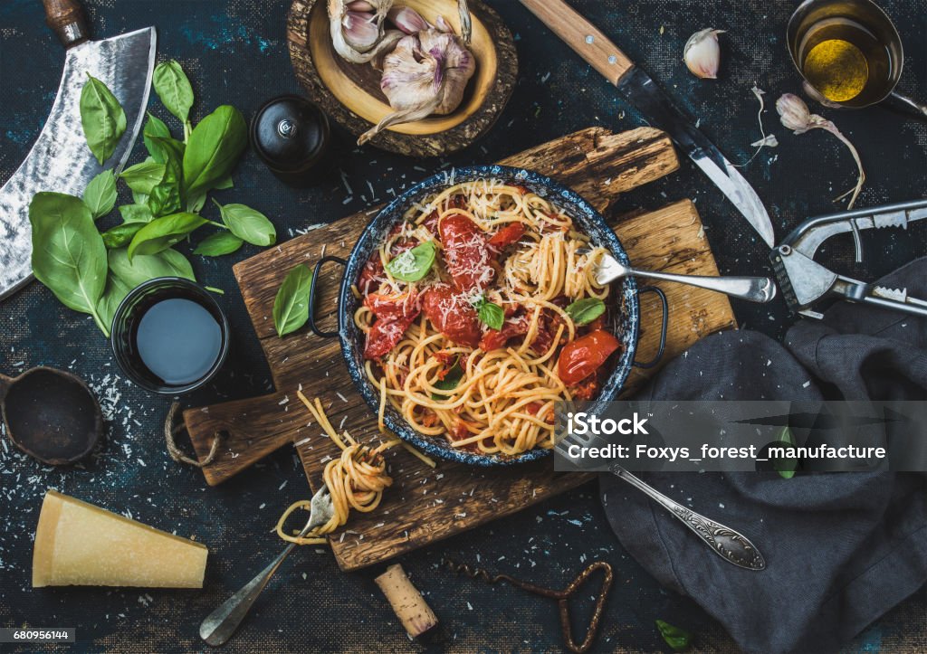 Spaghetti with tomato and basil and ingredients for making pasta Italian style pasta dinner. Spaghetti with tomato and basil in plate on wooden board and ingredients for cooking pasta over dark blue plywood background, top view Pasta Stock Photo