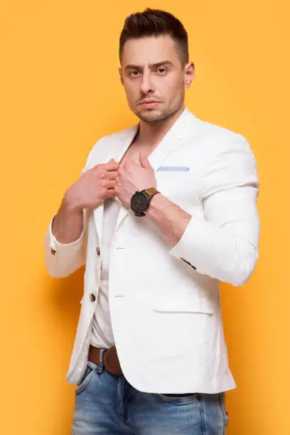 Handsome elegant man in white jacket standing on yellow background