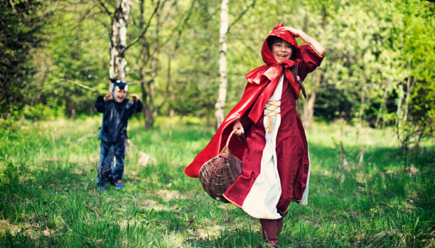 Little Red Riding Hood in red dress and famous red cape is having fun running from the tiny version of Big Bad Wolf. The red is about 8 years old and the wolf is 5 years old.\n