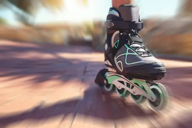 Closeup shot of a young woman's feet in rollerblades speeding down a park path
