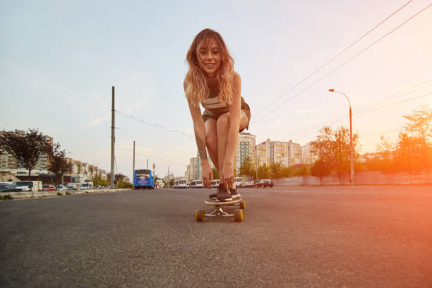 schöne junge mädchen mit tattoos reiten longboard bei sonnigem wetter - longboard skating stock-fotos und bilder